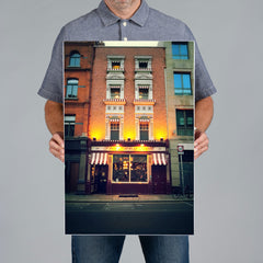 A man from The Canvas Works holds a large vertical 40x60cm cnavas print of a The Long Hall pub in Dublin at night. 