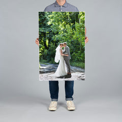 A person from The Canvas Works holding a large 60x90cm vertical printed photo on canvas of a bride and groom embracing on a forest path. 
