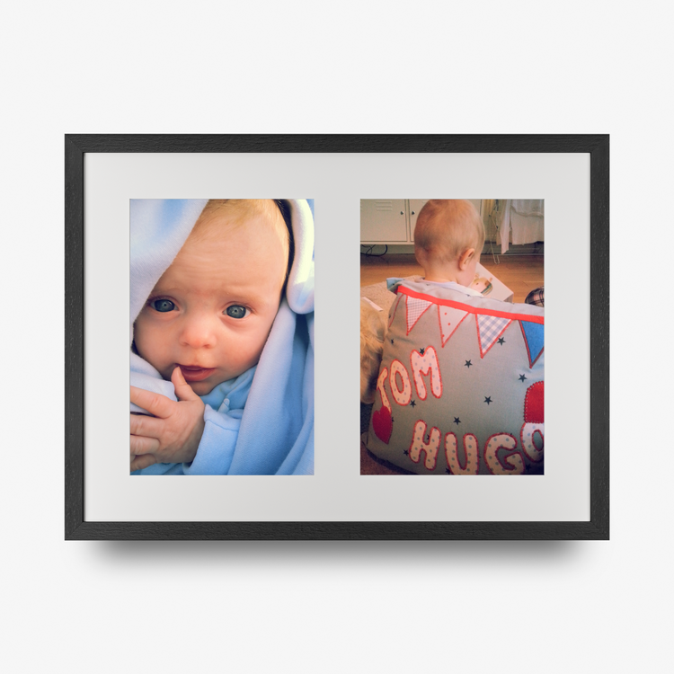 A double aperture multi photo framed print in a black frame featuring a photo of a blue eyed baby and a toddler with his back to the camera. 