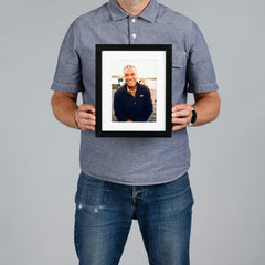 A man from The Canvas Works holds a 15x20cm black-framed custom portrait photo print against a solid gray background.