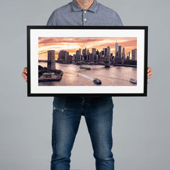 A person holding a 60x30cm framed panoramic print of a cityscape of the New York City skyline at sunset.