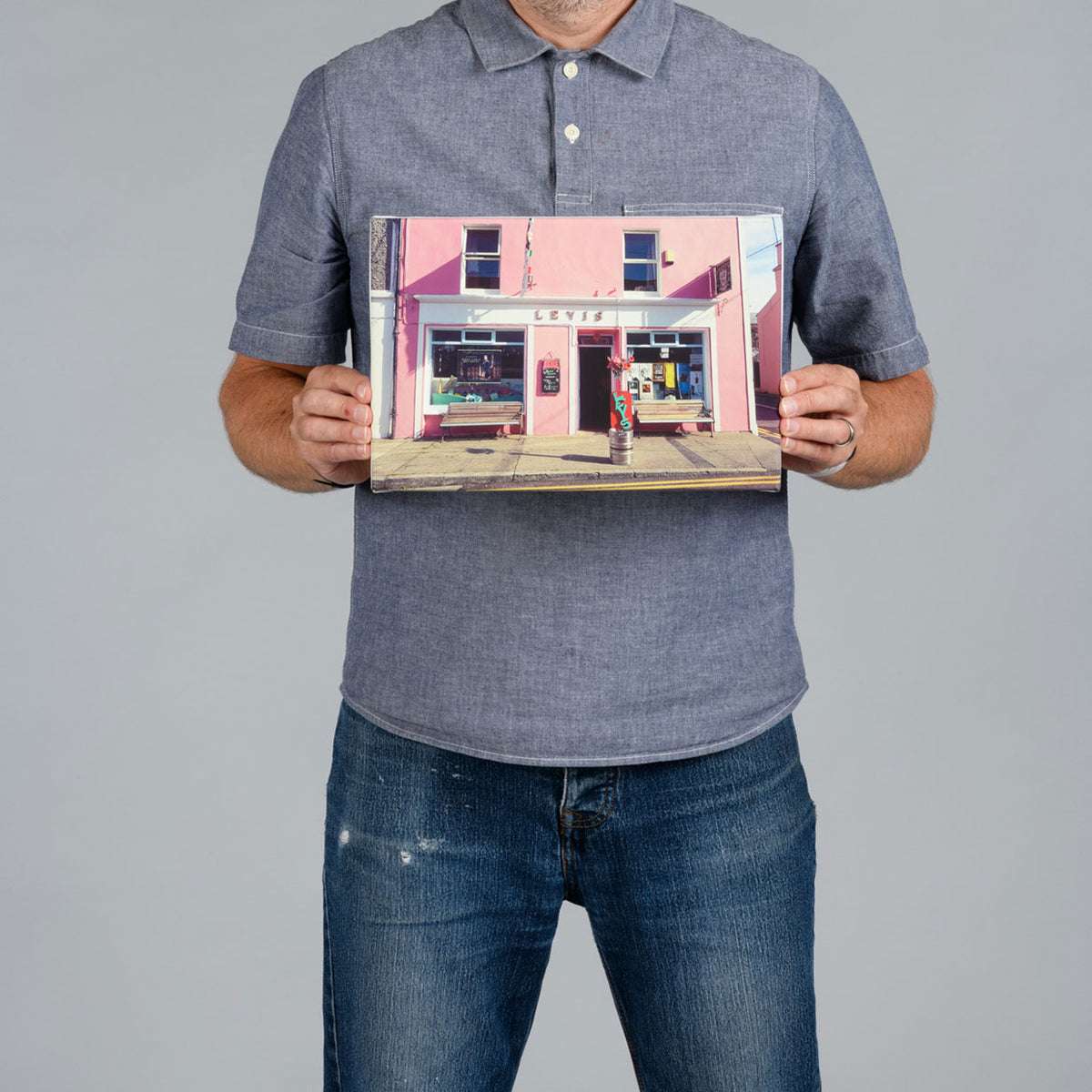 A man holding a landscape shape canvas print featuring Levis pub in Ballydehob