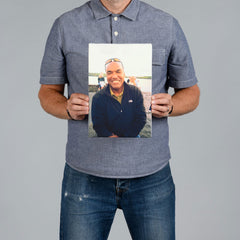 A man holding a portrait rectangle canvas print of a man sitting by the water